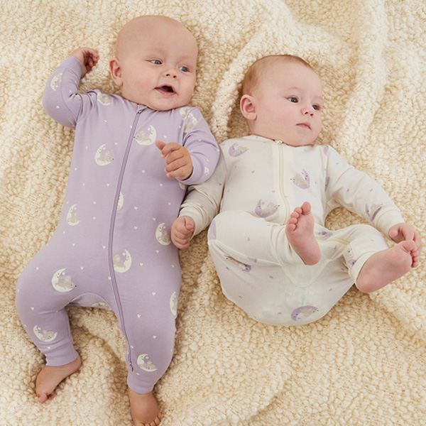 Två bebisar på en pläd klädda i pyjamas med tvåvägsdragkedja